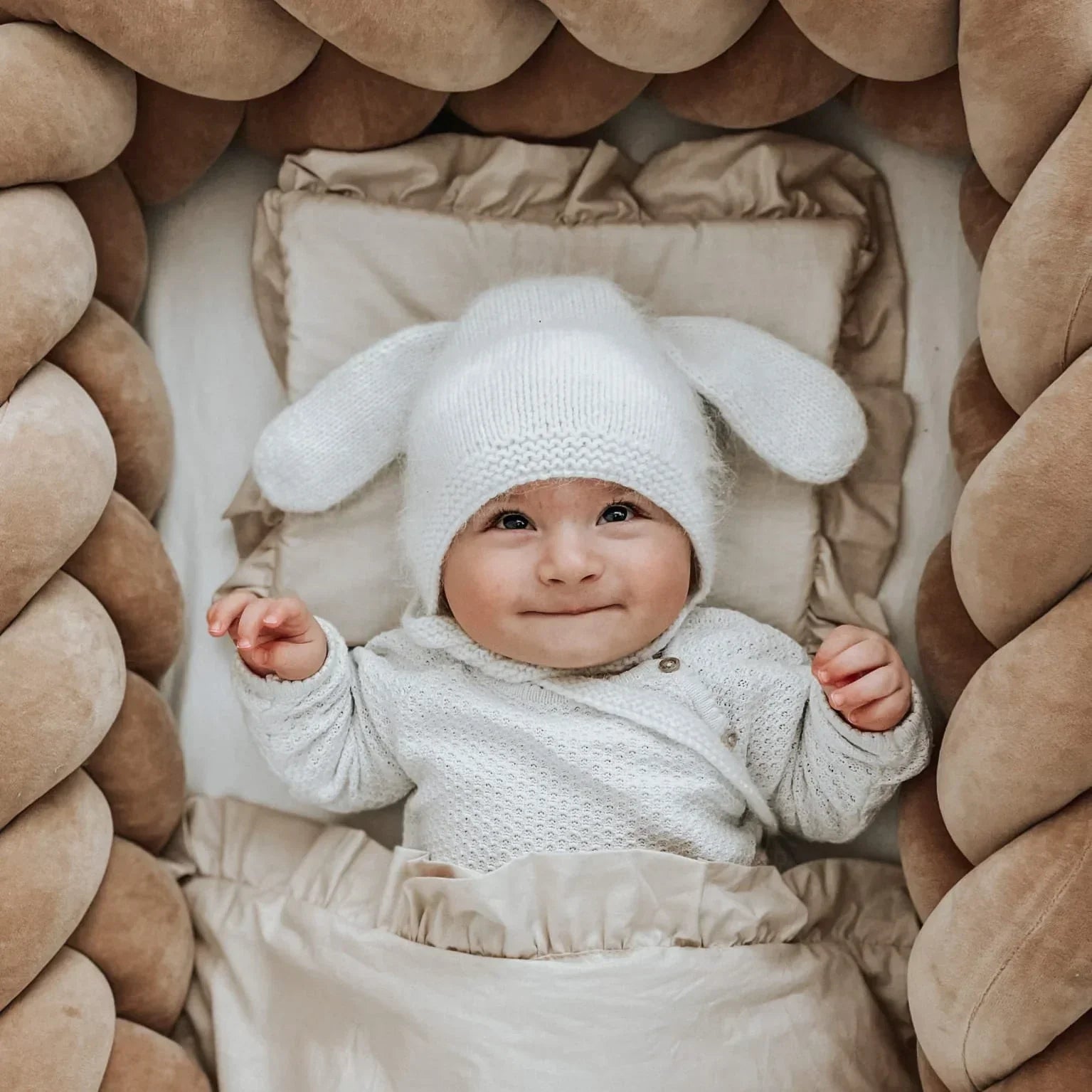 Bébé allongé dans un lit entouré d’une tresse de lit épaisse et moelleuse, offrant une protection douce et sécurisante, dans des tons naturels et chaleureux.