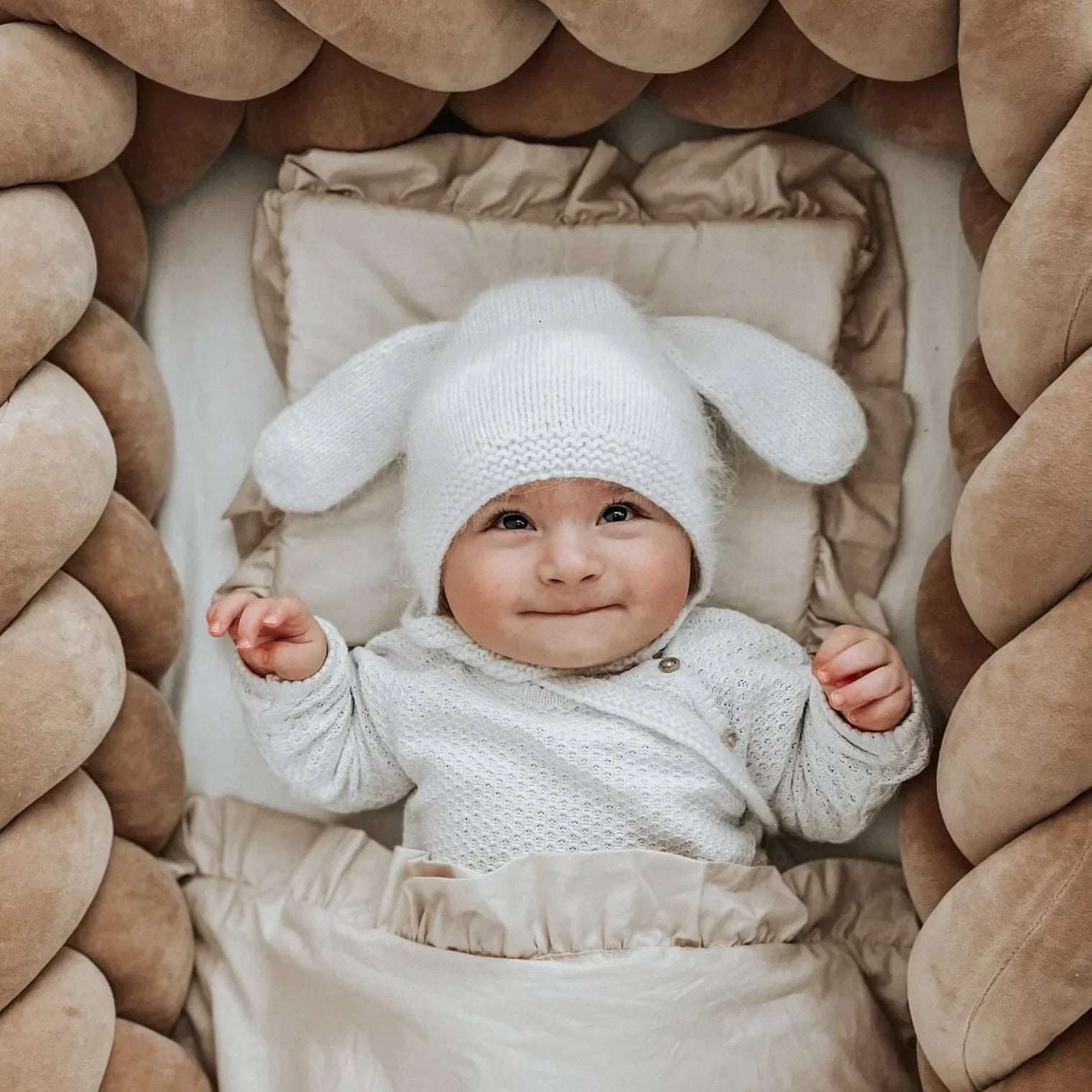 Bébé allongé dans un lit entouré d’une tresse de lit épaisse et moelleuse, offrant une protection douce et sécurisante, dans des tons naturels et chaleureux.